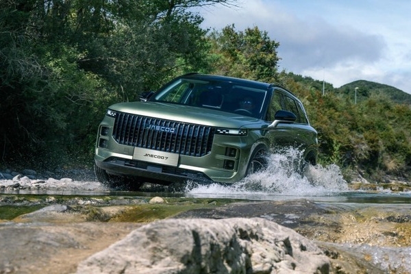 Green JAECOO 7 driving through a river with trees in the background