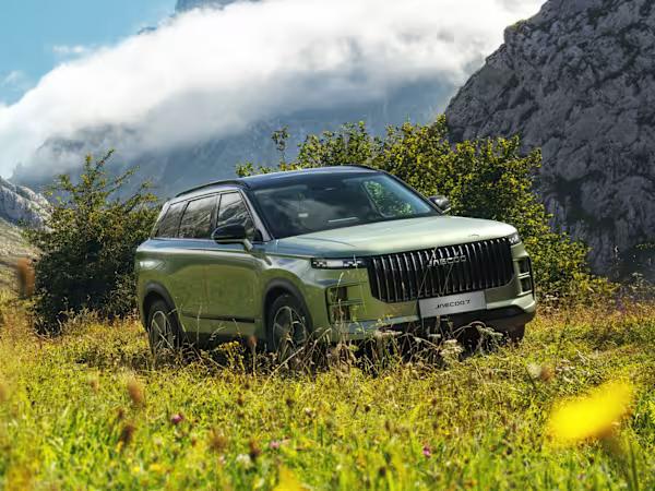 JAECOO 7 SHS car parked in a grassy field surrounded by mountains and clouds