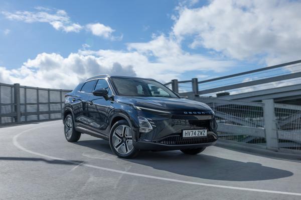 A sleek black OMODA E5 SUV driving on an elevated road under a partly cloudy sky, with a modern bridge structure in the background.