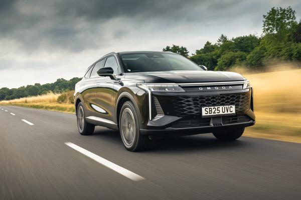 Black OMODA 9 SUV driving on a rural road with grassy fields and trees under a cloudy sky.