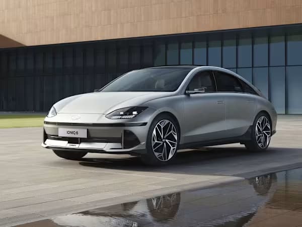 Silver Hyundai IONIQ 6 parked in front of a modern building, the car is reflected in a nearby puddle